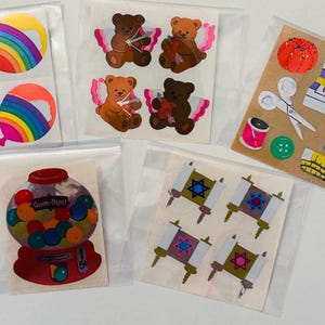 May include: A collection of colorful stickers in plastic sleeves. Designs include rainbow balloons, teddy bears with angel wings, sewing supplies, a gumball machine with the text "Gum-Bye!", and Torah scrolls.