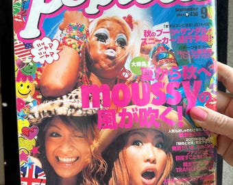 May include: A September 2001 issue of Popteen magazine featuring a bright, colourful cover with bold white text, multiple Japanese headlines, and photographs of three individuals with distinct makeup and hairstyles, surrounded by various graphic icons.
