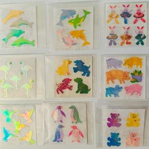 Pode incluir: Uma coleção de folhas de autocolantes coloridos com vários desenhos de animais. Os autocolantes incluem golfinhos, coelhos, cães, flamingos, porcos, beija-flores, pinguins e ursinhos de peluche. Cada folha é embalada individualmente numa manga de plástico transparente.