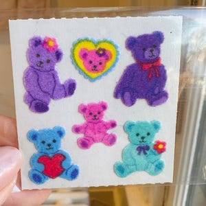 May include: A sheet of stickers featuring nine colorful teddy bears. The bears are in various poses, including sitting, standing, and holding hearts. The stickers are perfect for adding a touch of whimsy to any project.