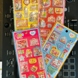 May include: Three rectangular sheets of colorful puffy stickers featuring various miniature illustrations of toys, accessories, and characters. Each sheet has a header with Japanese text and a hole for hanging, displaying diverse designs.