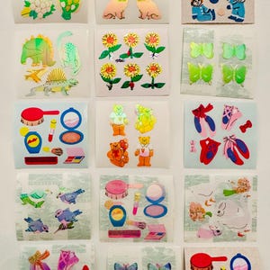 May include: A collection of vintage stickers featuring various designs. The stickers include images of flowers, cats, children in winter clothes, dinosaurs, butterflies, makeup items, teddy bears, and ballet shoes. The stickers are on a white background.