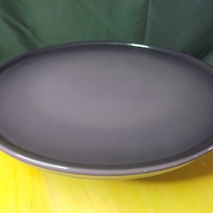 Op de afbeelding: Een grote, ronde, paarse keramische serveerschaal. De schaal heeft een gladde, glanzende afwerking en een licht verhoogde rand.