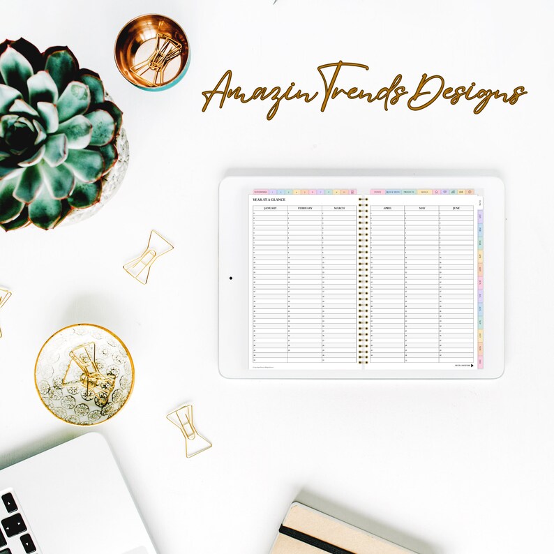 May include: A white tablet with a colorful weekly planner open to the "Week at a Glance" page. The planner has a gold spiral binding and is on a white surface with gold paper clips and a succulent plant.
