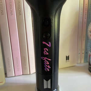 Peut inclure: Un b&acirc;ton lumineux noir avec une base argent&eacute;e et une sangle noire. Le b&acirc;ton lumineux a un bouton argent&eacute; et un autocollant rose et violet qui dit "7 es fate".