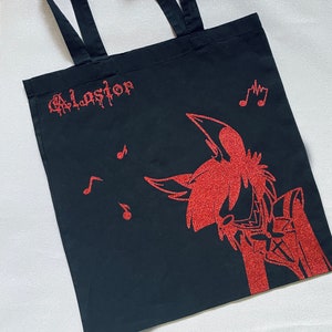 Könnte beinhalten: Schwarze Tragetasche mit roter Glitzerbeschriftung "Alastor" und einer roten Glitzerillustration einer Comicfigur mit Musiknoten.
