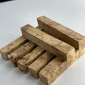 May include: A stack of six wooden blanks for turning, with a light brown color and a unique burl pattern. The blanks are rectangular in shape and have a smooth, polished finish.