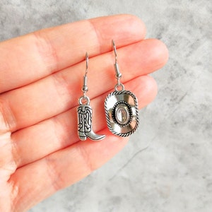 May include: A pair of silver dangle earrings with a cowboy boot charm on one earring and a cowboy hat charm on the other earring.