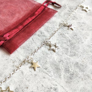 May include: A silver chain bracelet with multiple star charms hanging from it. The bracelet is lying on a grey textured surface.
