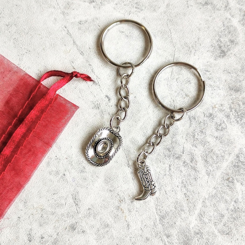 May include: Two silver keychains with charms. One charm is a silver cowboy hat and the other is a silver cowboy boot.
