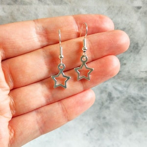 May include: A pair of silver star-shaped earrings with a simple, minimalist design. The earrings are small and delicate, with a hollow star shape.