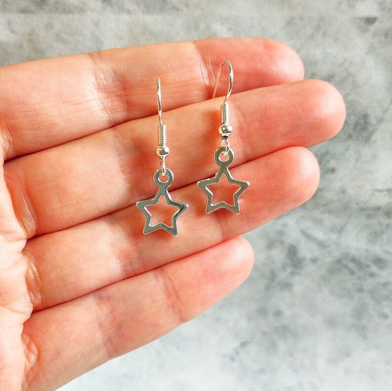 May include: A pair of silver star-shaped earrings with a simple, minimalist design. The earrings are small and delicate, with a hollow star shape.
