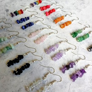 May include: Assortment of gemstone earrings with silver hooks. The earrings feature various colors and shapes of gemstones, including amethyst, rose quartz, black onyx, and green aventurine.