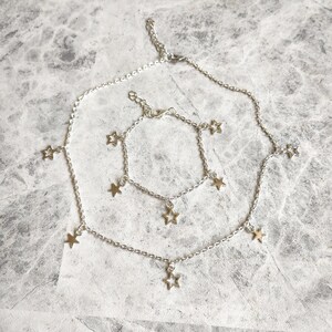 May include: A silver chain necklace and bracelet set with star charms. The necklace is longer than the bracelet and both have multiple star charms hanging from the chain.