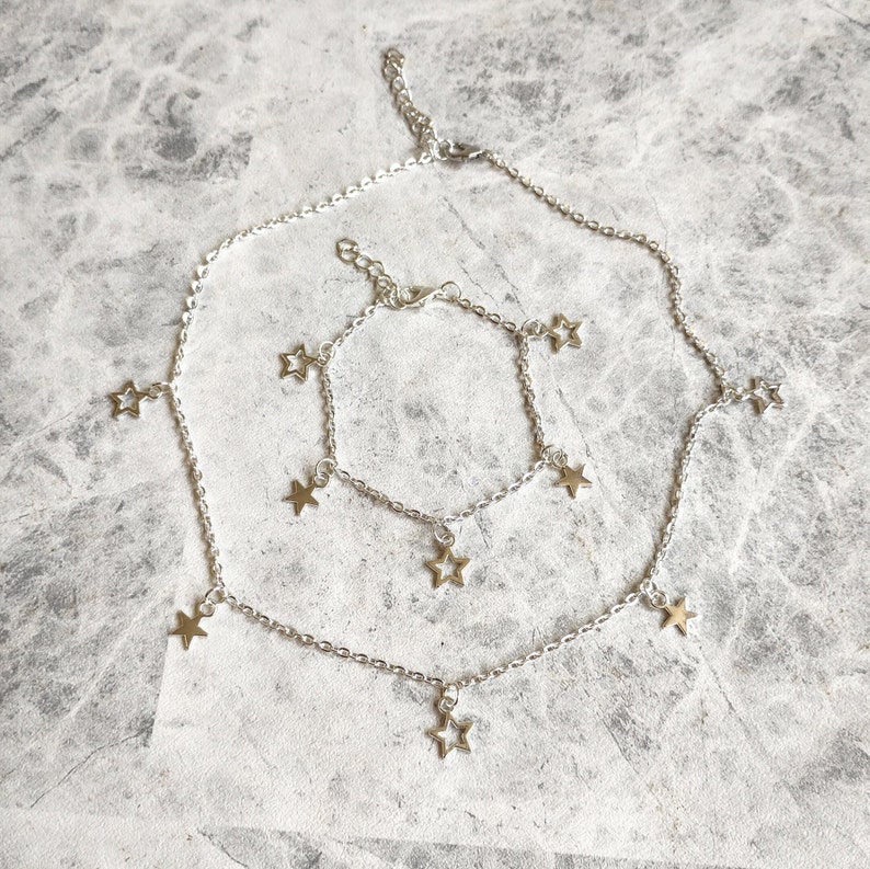 May include: A silver chain necklace and bracelet set with star charms. The necklace is longer than the bracelet and both have multiple star charms hanging from the chain.