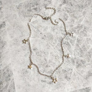 May include: A silver chain necklace with five dangling star charms. The stars are hollow and have a delicate, openwork design.
