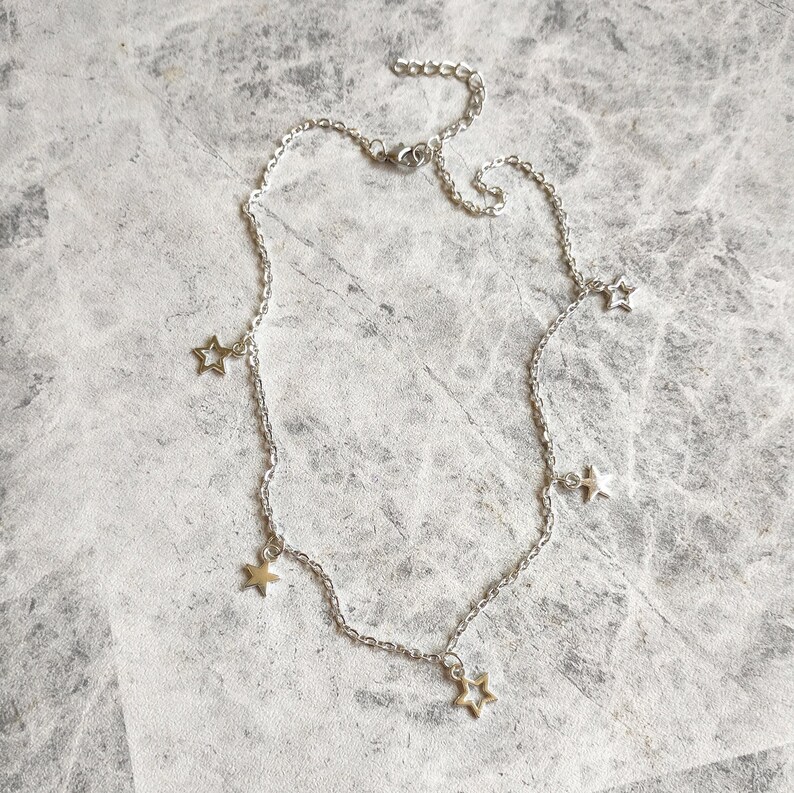 May include: A silver chain necklace with five dangling star charms. The stars are hollow and have a delicate, openwork design.