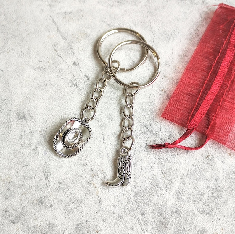 May include: A silver keychain with a cowboy hat and a boot charm. The keychain is attached to a red mesh bag.