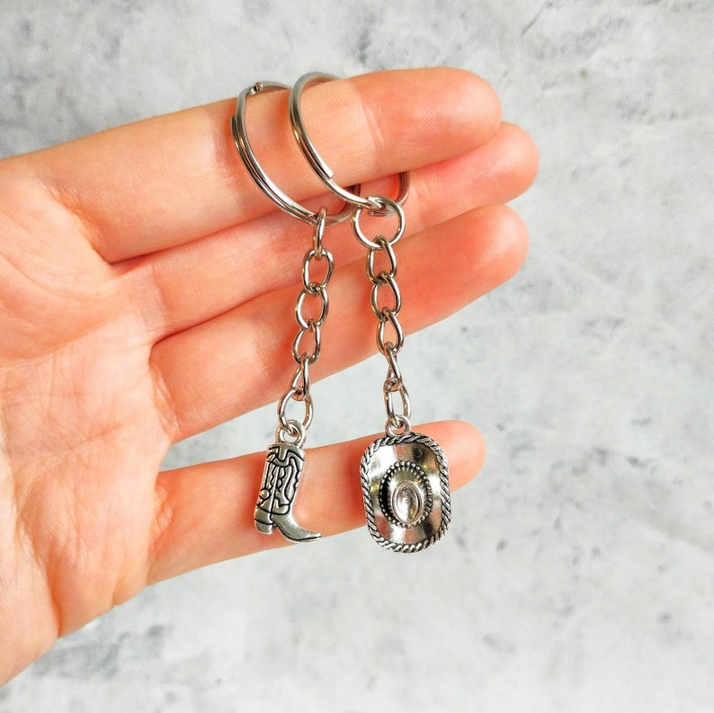 May include: Two silver keychains with charms. One charm is a cowboy boot and the other is a cowboy hat.