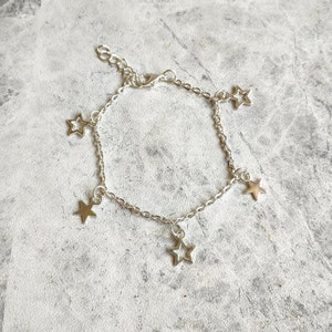 May include: A silver chain bracelet with five dangling star charms. The stars are hollow and have a simple design.