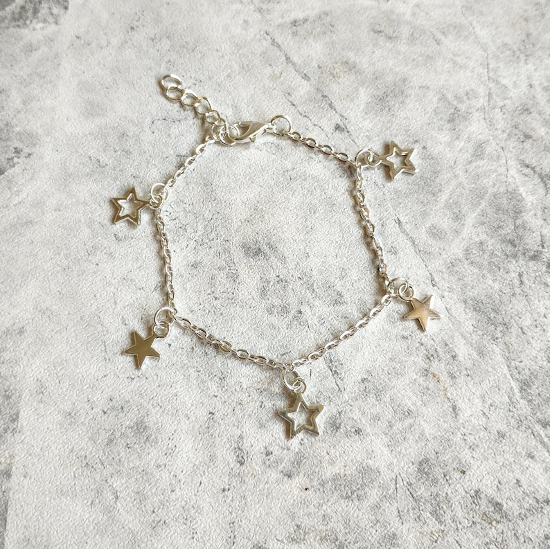 May include: A silver chain bracelet with five dangling star charms. The stars are hollow and have a simple design.