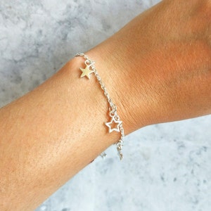 May include: A silver chain bracelet with two star charms. One star charm is solid and the other is open.