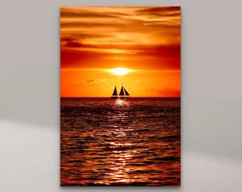 May include: A canvas print depicting a sailboat on the ocean at sunset. The sky is a vibrant orange and red, with the sun setting on the horizon. The water reflects the colors of the sky. The print is displayed on a wooden stand.