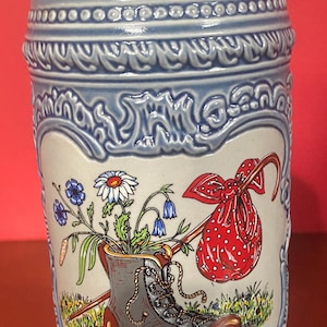 May include: A blue and white ceramic beer stein with a detailed floral design and a boot with flowers in it. The stein has the text "SV Allendorf 1986" on the front.