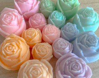 Puede incluir: Una colección de 14 jabones en forma de rosa de color pastel en varios tonos de rosa, verde, morado y naranja. Los jabones están dispuestos en un patrón circular sobre una superficie de madera clara.