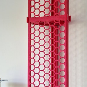 Puede incluir: Una estantería roja de dos niveles con un patrón de panal. La estantería está hecha de plástico y tiene un diseño moderno.