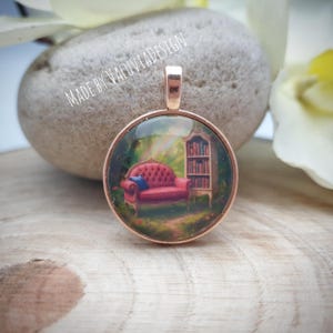 Könnte beinhalten: Ein runder Anhänger mit roségoldenem Finish. Der Anhänger zeigt ein Miniaturgemälde eines roten Sofas, eines Bücherregals und eines Regenbogens in einer Waldszene. Der Text "MADE BY VALUVIADESIGN" ist sichtbar.
