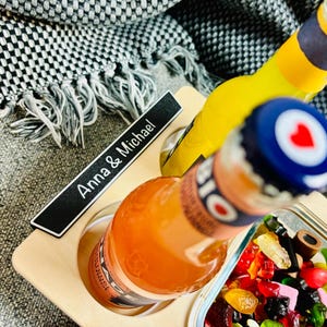 May include: A wooden serving tray with two bottles of soda and a small dish of colorful candies. The bottles are orange and yellow, with blue and white bottle caps. The tray has the text "Anna & Michael".