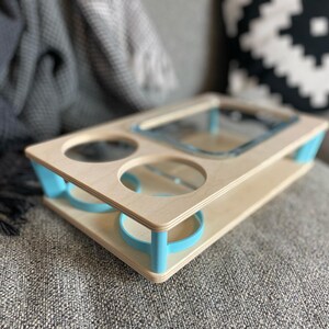 May include: A wooden serving tray with a light blue trim and accents. The tray has cutouts for two glasses, a square dish, and a round dish. The tray is made of light-colored wood and is designed to hold drinks and snacks.
