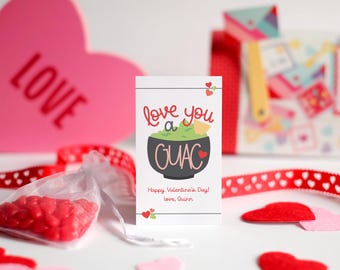 Op de afbeelding: Een witte kaart met de tekst "Love you a Guac" in rode en zwarte letters. De kaart bevat ook een cartoonillustratie van een kom guacamole met een rood hart en een tortillachip. De tekst "Happy Valentine's Day! Love, Quinn" staat onder de illustratie.