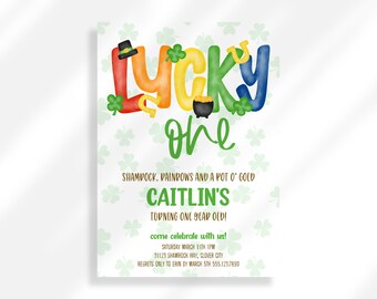 May include: A colorful invitation for a first birthday party with a St. Patrick's Day theme. The invitation features the words "Lucky One" in rainbow colors with shamrocks, a pot of gold, and a horseshoe. The text reads "Shamrock, Rainbows and a Pot o' Gold Caitlin's Turning One Year Old! Come celebrate with us! Saturday March 11th 1 PM 31123 Shamrock Way, Clover City Regrets only to Erin by March 5th 555.123.7890"