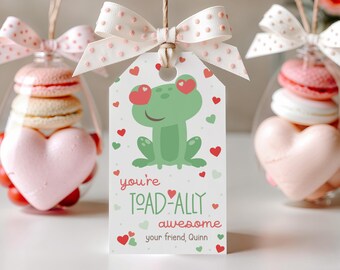 Peut inclure: Une étiquette cadeau blanche avec une grenouille verte portant des lunettes en forme de cœur rouge. L'étiquette indique "you're toad-ally awesome" et "your friend, Quinn".