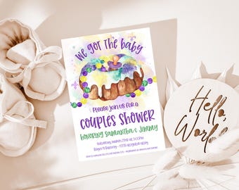 Pode incluir: Um convite em aquarela roxo e verde para um chá de bebê de casais. O convite apresenta um bolo de reis com cobertura roxa, verde e dourada e uma chupeta de bebê no topo. O texto do convite diz: "We got the baby. Please join us for a couples shower honoring Samantha & Jimmy. Saturday, March 22nd at 3:00PM. Berger's Bakery - 11775 Alligator Alley."