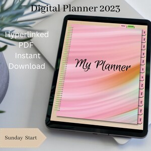 May include: A digital planner for 2023 with a pink and orange gradient background. The planner has a tabbed calendar section and a notes section. The text "My Planner" is written in black cursive on the cover. The text "Sunday Start" is written in black on a white background with a brown border.