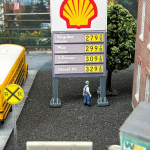 Puede incluir: Un modelo en miniatura de un letrero de gasolinera con el logotipo de Shell. El letrero muestra los precios de la gasolina regular, plus, V-Power y diésel. Los precios son 2,79, 2,99, 3,09 y 3,29 por litro.