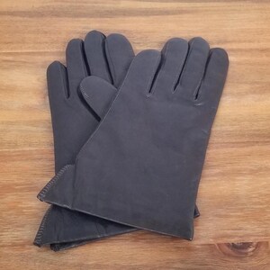 Puede incluir: Un par de guantes de cuero gris oscuro. Los guantes están superpuestos, con los dedos apuntando hacia arriba. Los guantes tienen una textura suave y probablemente son para el frío.