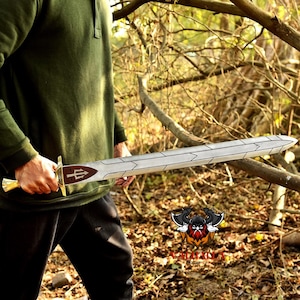 May include: A silver and gold sword with a brown handle and a trident symbol. The sword has a long, straight blade with a decorative design. The handle is gold with a brown inlay. The sword is held by a person wearing a green shirt.