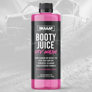 May include: Pink bottle of UTV wash with the text "BOOTY JUICE UTV WASH" on the label. The bottle is labeled with the brand name "BRAAAP MOTO" and the text "FOAM CANNON OR BUCKET USE, HIGH SUD CONTENT, POWERFUL CLEANING, CONCENTRATED FORMULA, FOR ALL OFFROAD/ONROAD VEHICLES, WWW.BRAAAPMOTO.COM, NET CONTENTS: 16 FL OZ. (473ML)".