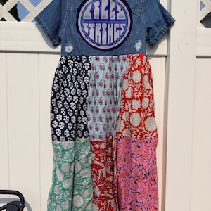 May include: A short-sleeved denim dress featuring a circular patch on the back with the text Billy Strings. The skirt is constructed from various patchwork fabric panels in navy, light blue, red, and pink with floral and botanical patterns.