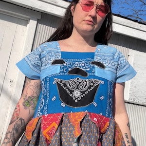 May include: A blue patchwork dress with a square neckline and short sleeves. The top is made from blue bandanas, with a black and white bandana design on the front. The skirt has a patterned design with red and orange accents.