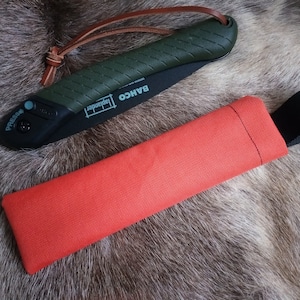 May include: A green and black folding saw with a leather strap and a red canvas sheath with a black strap. The saw has the text "BAHCO" and "Japander" printed on it.