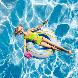 May include: A doll wearing a lime green outfit and purple headphones floats on a striped inflatable ring in a pool. The doll holds a pink boombox. The water is a bright blue with sunlight reflections.