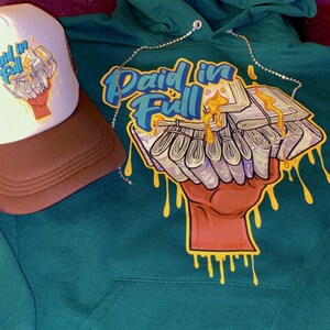 May include: A green hoodie with a graphic of a hand holding a stack of money with the text "Paid in Full" in blue and yellow lettering. A brown and white trucker hat with the same graphic is also included.