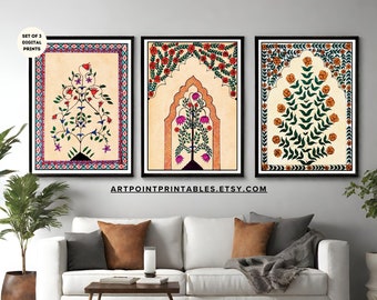 May include: Set of three digital prints featuring traditional Indian art. Each print depicts a stylized tree with flowers and leaves in a colorful archway. The prints are framed in black and displayed on a white wall above a white couch.