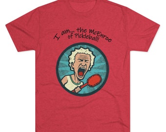 May include: Red t-shirt featuring a cartoon image of a man with white hair shouting while holding a pickleball paddle. The text "I am... the McEnroe of Pickleball!" is printed on the shirt.