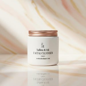 May include: A white jar with a rose gold lid, labelled "Tallow & Oil FACIAL CLEANSER." The jar contains 113 grams of product and features the website renderedradiance.com. The background has a soft, marbled pattern.